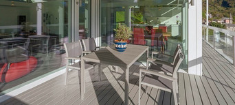 Überdachte Terrasse mit grauem Holzboden, modernem Esstisch-Set und Blick in den offenen Wohnbereich.