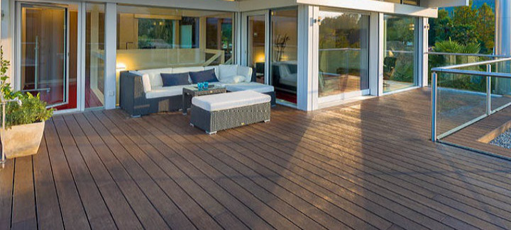 Moderne Terrasse mit dunklem Escheholz-Belag, stilvoller Rattan-Lounge mit weißen Polstern und direktem Zugang zum Wohnbereich.
